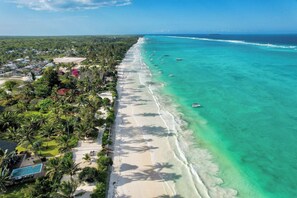 Vista aérea de una zona costera con playa, aguas turquesas cristalinas y una fila de barcos.