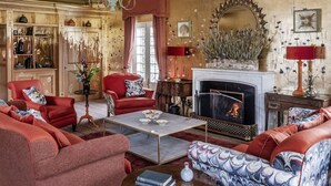 Una sala de estar tradicional con chimenea, muebles tapizados en rojo y un espejo decorativo.