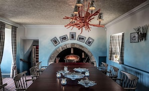 Uma sala de jantar com uma mesa comprida, cadeiras, lareira e um lustre singular.