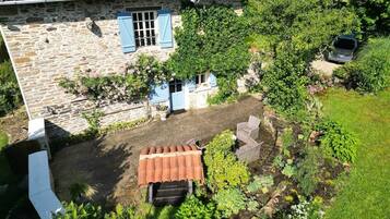 Uma casa de pedra com telhado de azulejos, um jardim com diversas plantas e um carro estacionado.