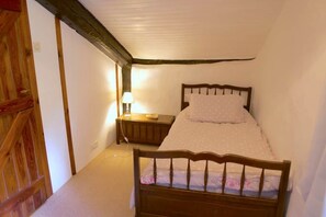 A small, cozy bedroom with a wooden bed, a nightstand with a lamp, and a wooden door. - Storybook Stone Cottage with Private Garden (Oradour-sur-Vayres)