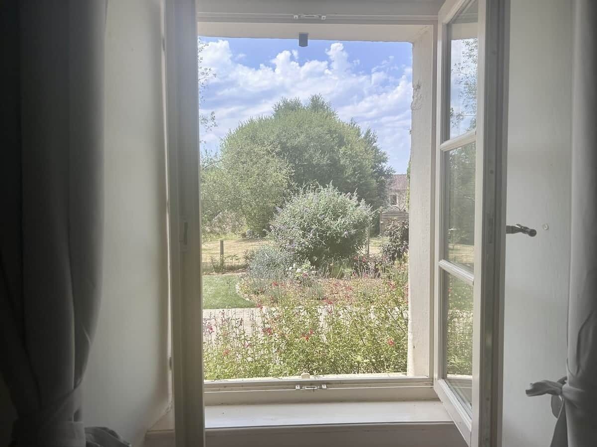 Une fenêtre ouverte donnant sur un jardin et un arbre.
