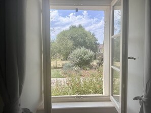 Una finestra aperta con vista su un giardino e un albero.