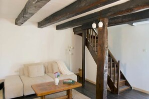 A living room with a sofa, a wooden table with a vase and book, and a staircase with wooden railings. - Storybook Stone Cottage with Private Garden (Oradour-sur-Vayres)