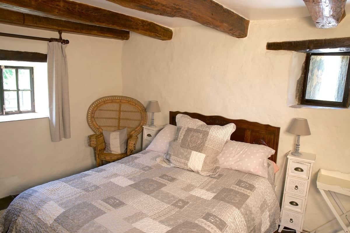 Quarto com cama, uma cadeira, mesa de cabeceira, luminária e janela.