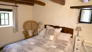 Quarto com cama, uma cadeira, mesa de cabeceira, luminária e janela.