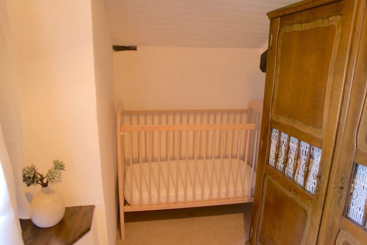 A room with a wooden crib, a wooden cabinet with decorative cut-out doors, and a small potted plant on a wooden shelf.