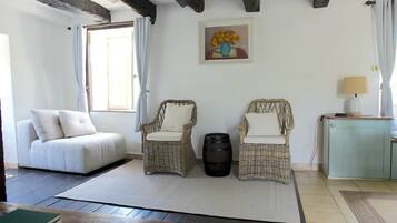 A room with a sofa, two wicker chairs, a table, a lamp, and a painting on the wall.
