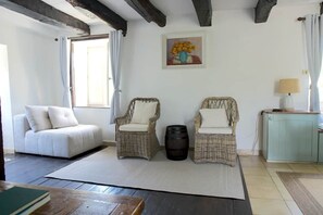 A room with a sofa, two wicker chairs, a table, a lamp, and a painting on the wall. - Storybook Stone Cottage with Private Garden (Oradour-sur-Vayres)