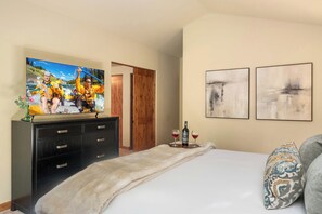 Ein Hotelzimmer mit einem Bett, einem Fernseher, der eine Rafting-Szene zeigt, einer Holztür und zwei abstrakten Bildern an der Wand.
