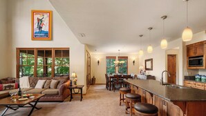 A spacious living area with a sofa, coffee table, and a dining table with chairs. There is a kitchen area with a bar and stools. - Abode at The Timbers, minutes to skiing, hot tub (Ketchum)