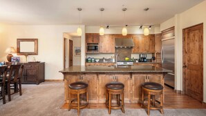 A kitchen with wooden cabinets, a central island with stools, a refrigerator, and pendant lighting. - Abode at The Timbers, minutes to skiing, hot tub (Ketchum)
