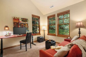 Ein gemütliches Zimmer mit Schreibtisch, Stuhl, Fernseher und einer Couch mit Decke.
