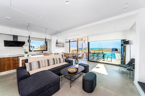 A modern living space with a kitchen, dining area, and a balcony with a pool view. - Kamelia Luxury Villa 2 (Crete)