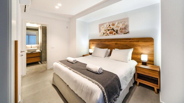 Une chambre d’hôtel moderne avec un grand lit, une tête de lit en bois, une table de chevet avec une lampe et un tableau au mur.