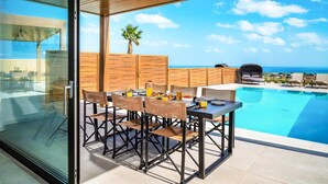 Un espace repas extérieur moderne, doté d’une piscine et offrant une vue sur l’océan.