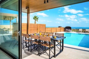 A modern outdoor dining area with a pool and a view of the ocean. - Kamelia Luxury Villa 2 (Crete)