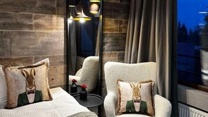 A modern hotel room with a large mirror, a plush armchair, a bed with decorative pillows, and a view of the outdoors. - Murgavets Hotel (Chepelare)