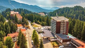 A hotel with multiple floors, a parking area, and a mountainous backdrop. - Murgavets Hotel (Chepelare)