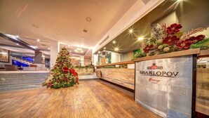A hotel lobby with a Christmas tree, wooden flooring, and a reception desk with the name 'SHARLOPOV Group'. - Murgavets Hotel (Chepelare)
