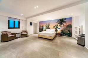Ein Schlafzimmer mit einem Bett, zwei Stühlen, einem kleinen Tisch, einem Kleiderschrank und einem Gemälde einer Sonnenlandschaft.