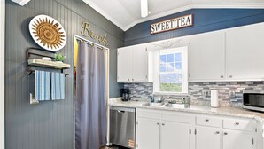 A kitchen with white cabinets, a stainless steel dishwasher, a microwave, and a window with a view. - Cozy Holden Beach dog friendly beach cottage. Only 1.4 miles to Holden Beach on mainland side. (Supply)