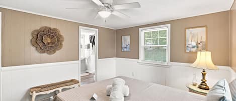 Un dormitorio con cama, una banca, un ventilador de techo, una ventana con persianas y una lámpara fijada a la pared.