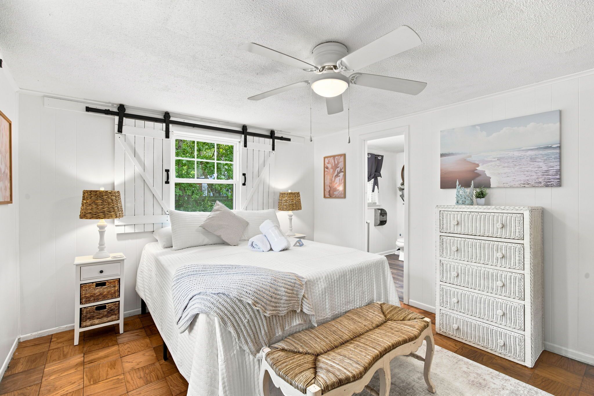 A bedroom with a bed, bedside tables, a bench, a ceiling fan, and a large window.