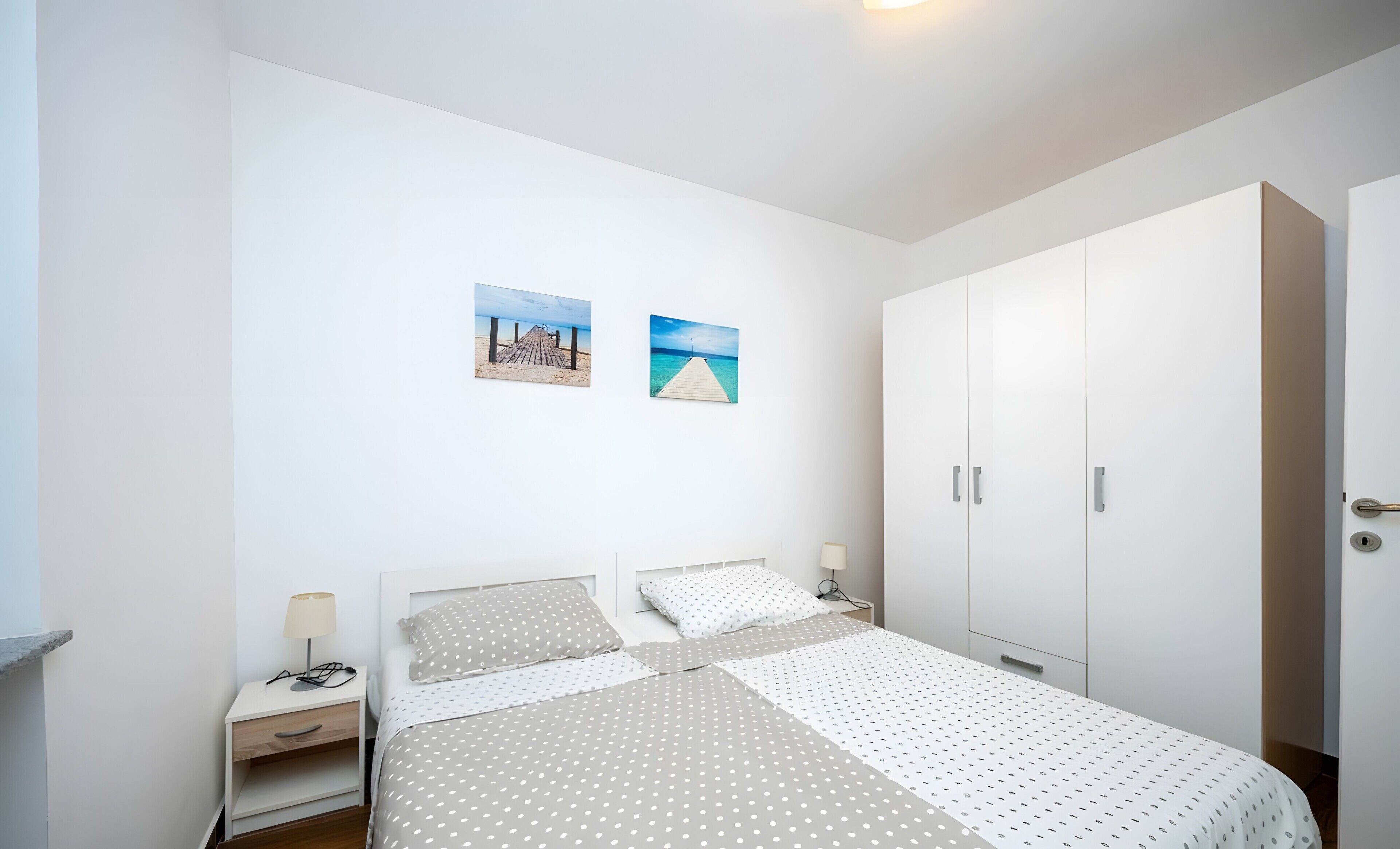 A bedroom with a bed, nightstands, a wardrobe, and two wall-mounted pictures.