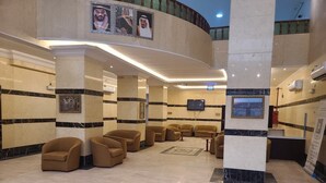 A lobby with a reception desk, seating area, and a large screen. - Qimmat AlAwali Hotel (Makkah)