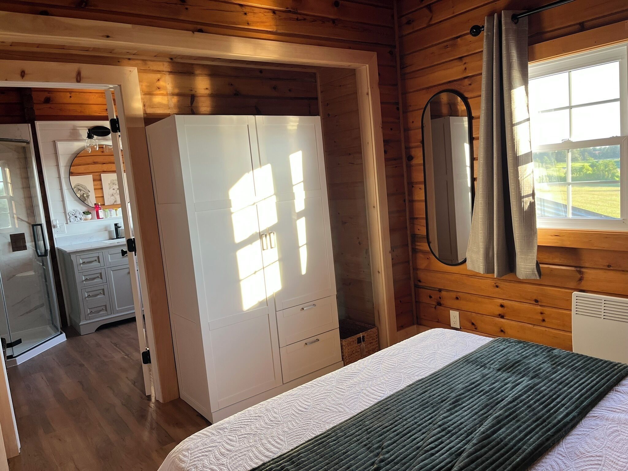 A bedroom with a bed, a wardrobe, a mirror, and a window with curtains.