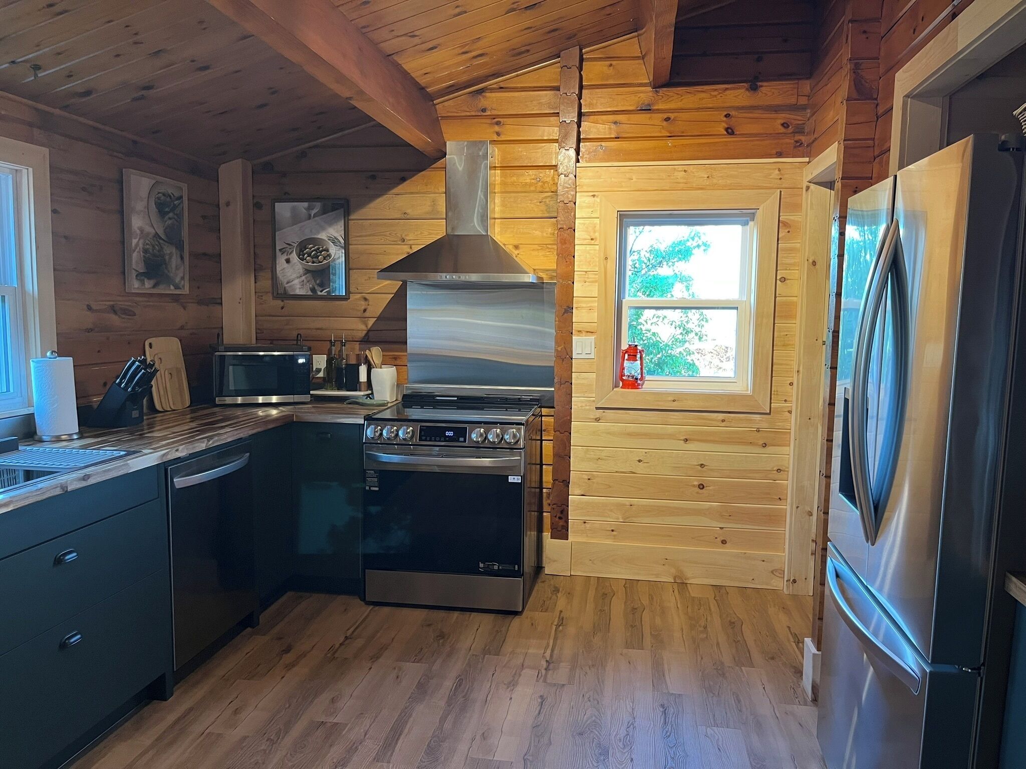A compact kitchen with wooden walls, a stove, a microwave, and a refrigerator.