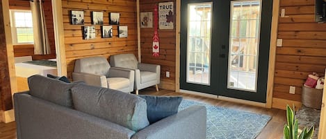 A cozy cabin interior with a grey sofa, two armchairs, a small table, and a potted plant.
