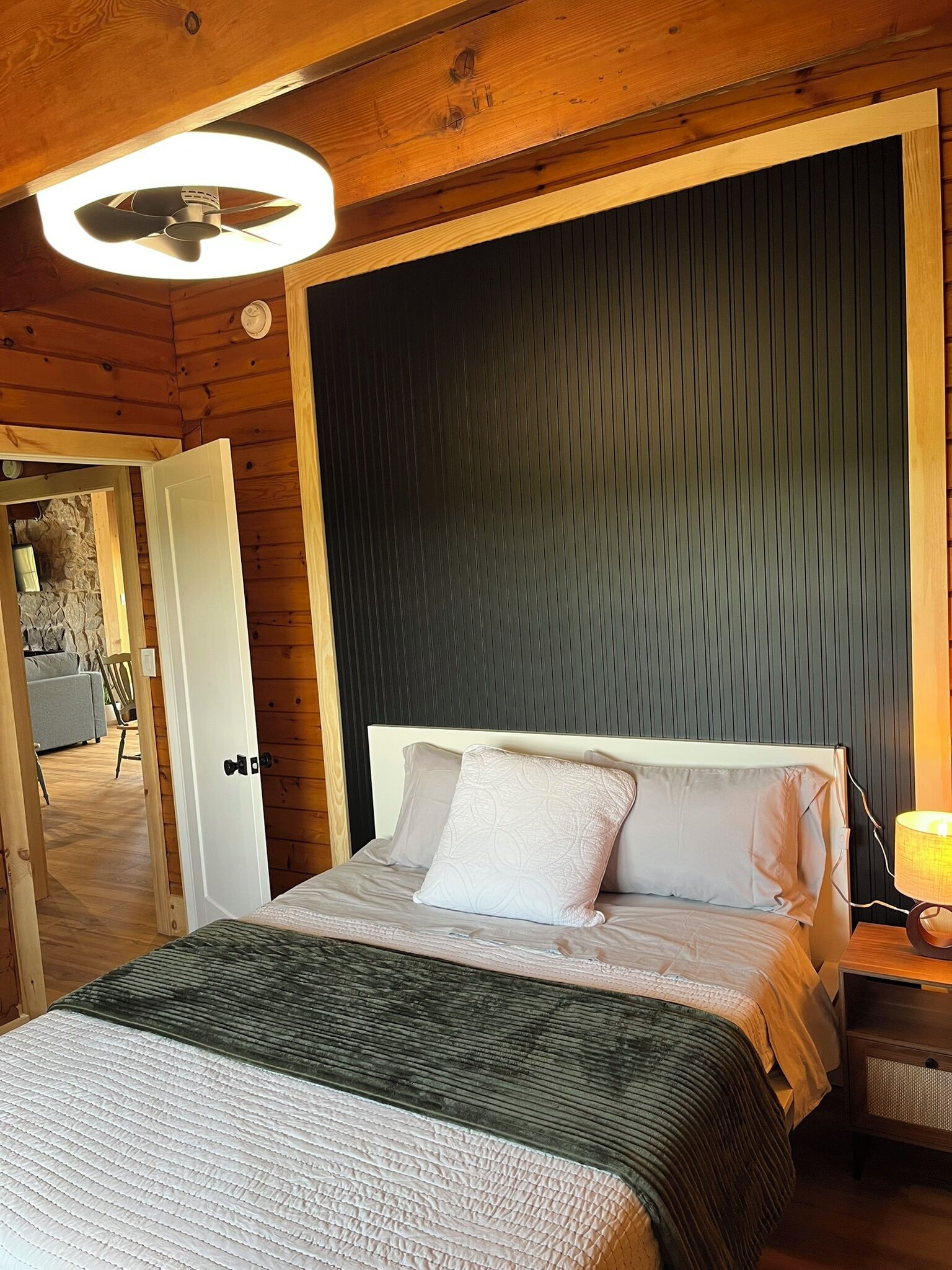 A wooden room with a bed, a nightstand, a lamp, and a ceiling fan.