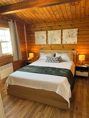 Une chambre dans un chalet en bois, avec un lit, deux lampes de chevet et trois tableaux accrochés au mur.