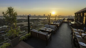 An outdoor dining area with tables and chairs, overlooking a cityscape during sunset. - Mekong View Apartment and Hotel II (Phnom Penh)