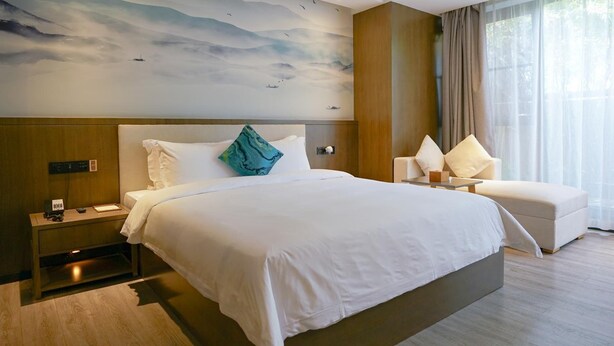 A modern hotel room with a large bed, a nightstand, a seating area, and a wall mural. - Paco Hotel (Guangzhou)