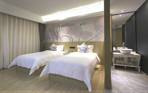 Et hotelværelse med to senge, et natbord, et stort spejl og et badeværelse med vask og håndklædestang.