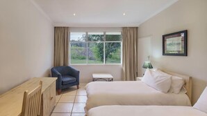 Habitación de hotel con dos camas, un escritorio, una silla, una ventana con cortinas y un cuadro en la pared.