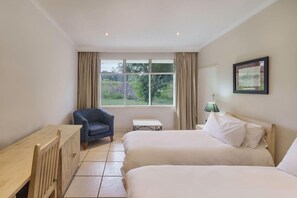 A hotel room with two beds, a small table, a chair, and a window with curtains.