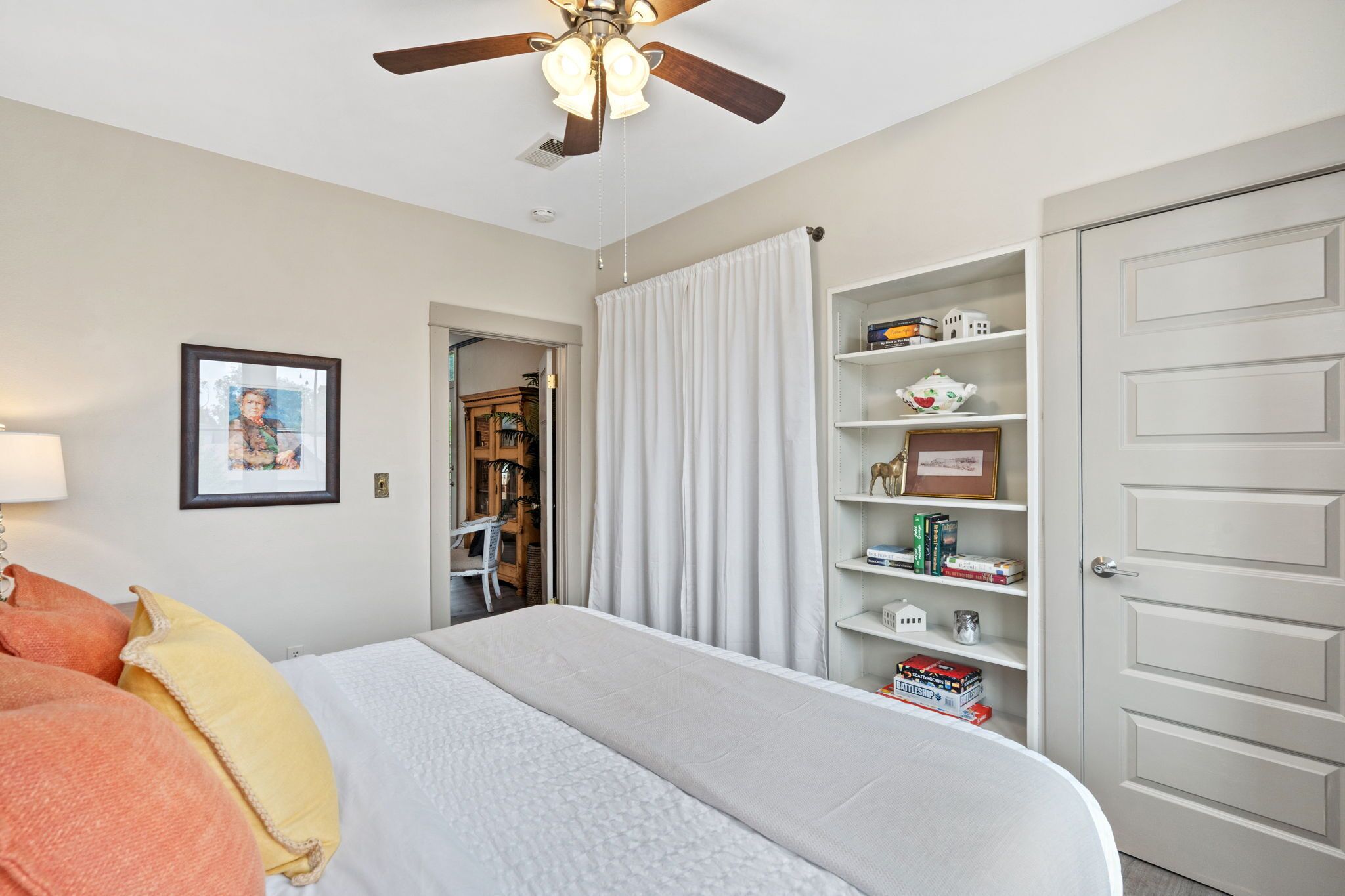 Un dormitorio con cama, ventilador de techo, estantería y puerta.