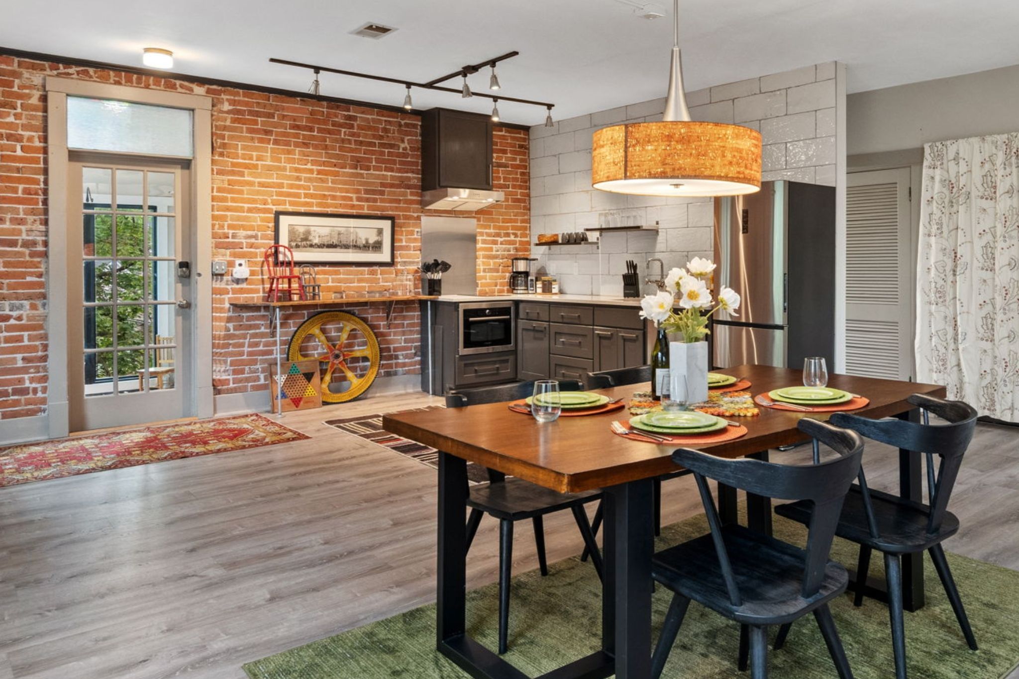 Una cocina moderna con pared de ladrillo, una zona de comedor con mesa y sillas de madera, y una lámpara colgante grande.