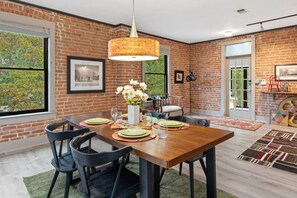 A dining area with a brick wall, a wooden table, and chairs. - Magnolia Market Loft | Steps to Old Town & Trails (Fort Collins)