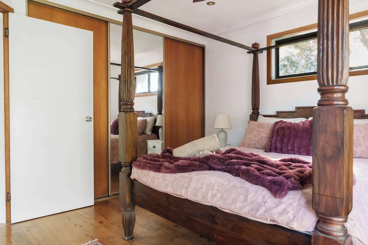 A four-poster bed with a wooden frame, a purple blanket, and a white pillow.