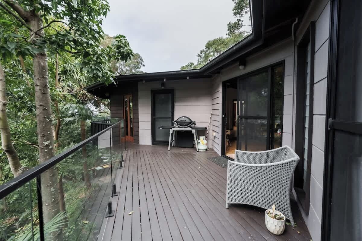 Une terrasse en bois avec une balustrade en verre, une chaise en osier et une table avec des chaises.