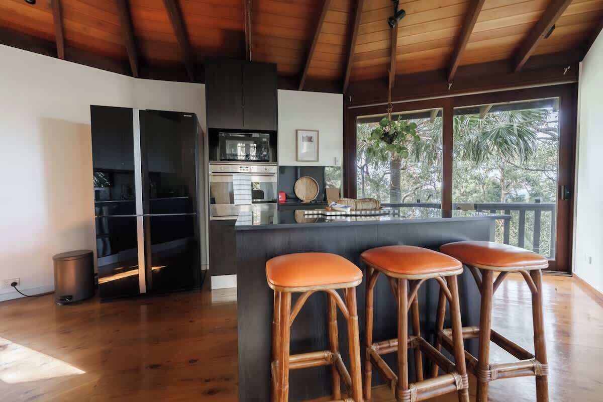 A modern kitchen with a central island, bar stools, and a view of the outdoors.