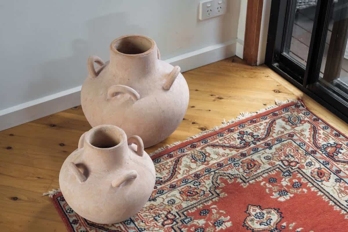 Deux pots en céramique sur un plancher en bois, avec un tapis à motifs.