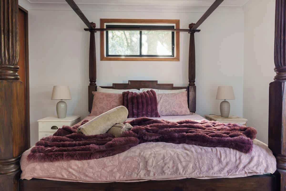 A bedroom with a four-poster bed, a window above the bed, and two bedside tables with lamps.