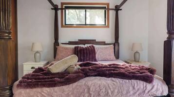 A bedroom with a four-poster bed, a window above the bed, and two bedside tables with lamps.