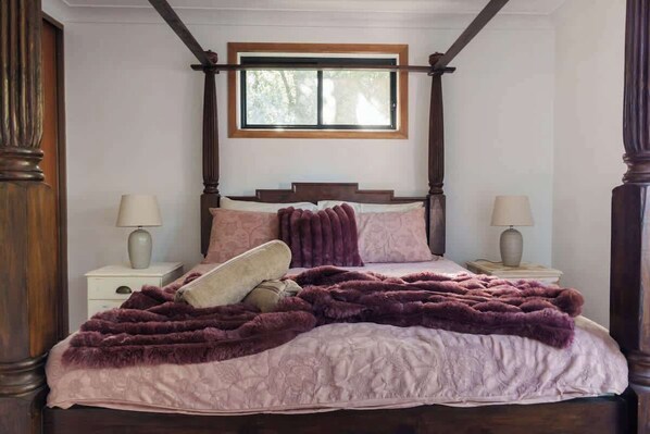 Une chambre à coucher avec un lit à baldaquin, une fenêtre située au-dessus du lit et deux tables de chevet avec des lampes.